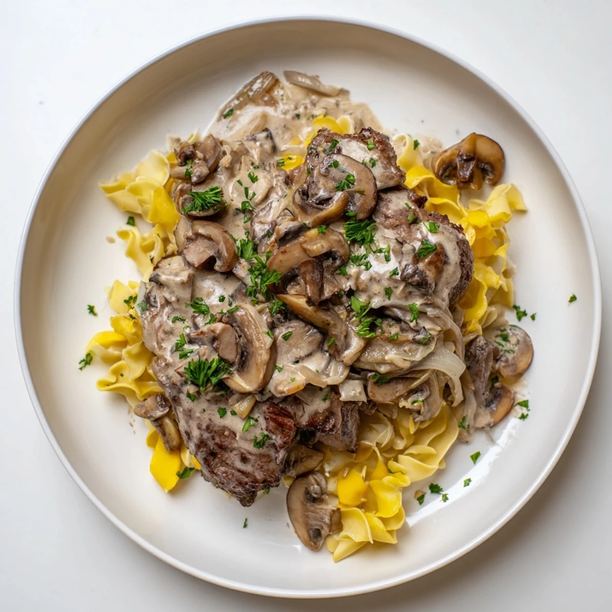 Delicious and flavorful beef stroganoff, garnished with parsley, served over warm, buttery egg noodles.