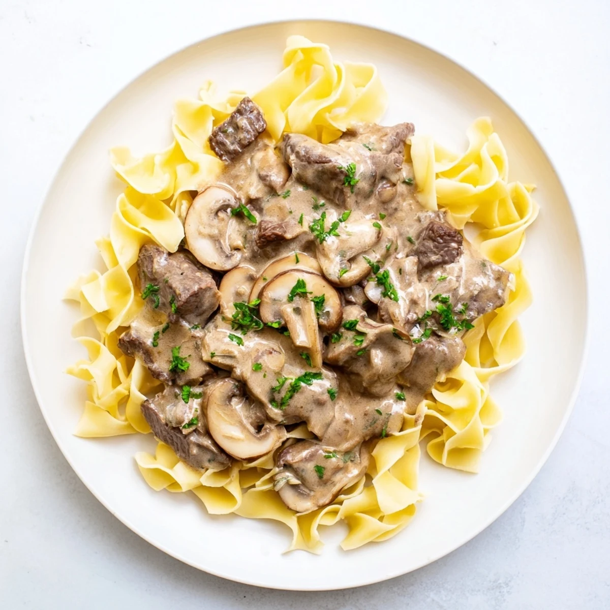 Tender beef strips in a rich sauce, spooned over perfectly cooked egg noodles in a Beef Stroganoff dish.