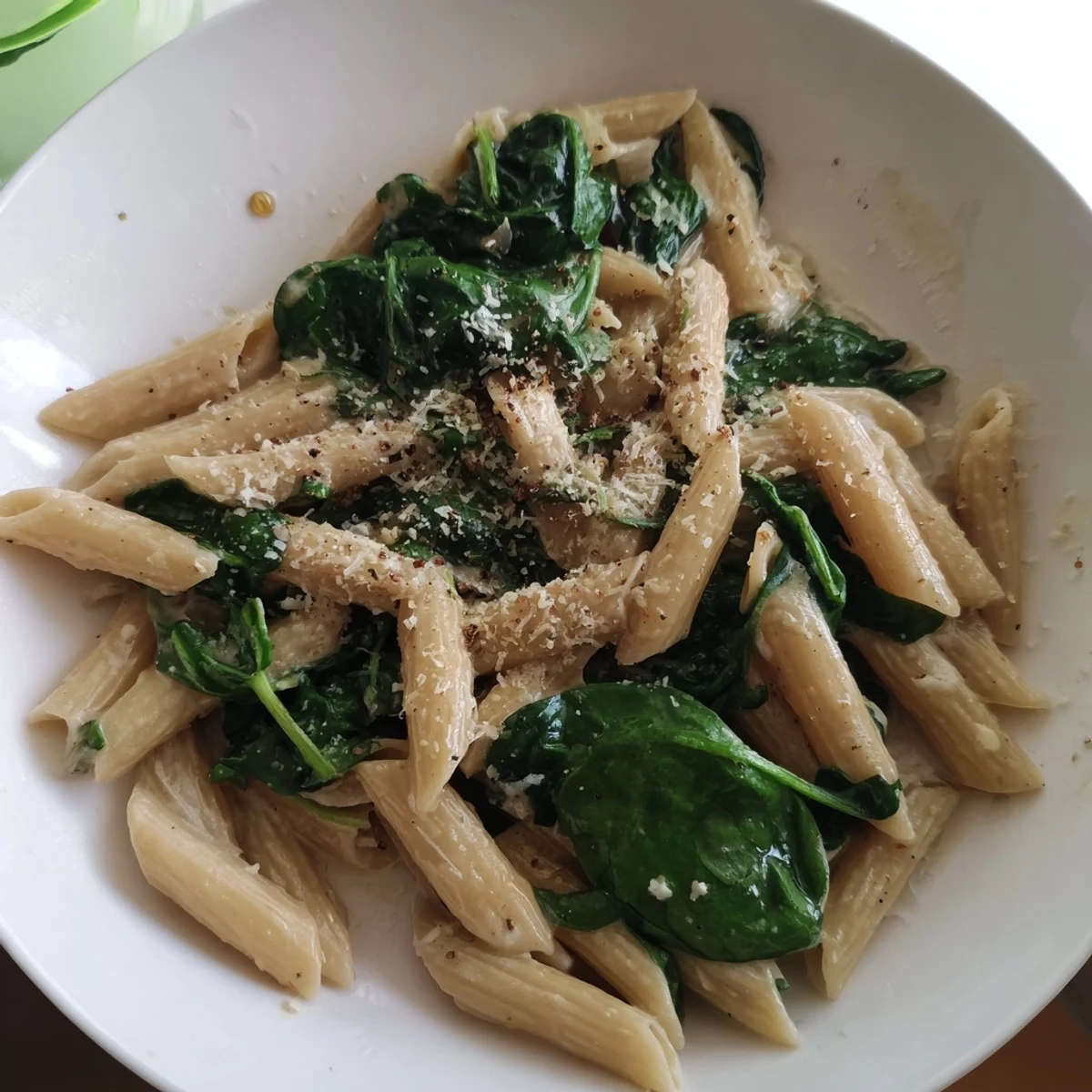 A vibrant bowl of creamy spinach pasta, garnished with fresh parsley and extra Parmesan cheese.