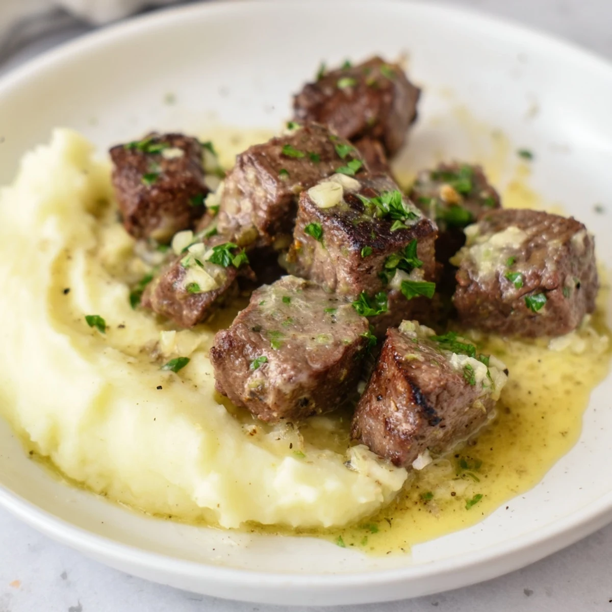 Close-up of juicy Garlic Butter Steak Bites and fluffy mashed potatoes garnished with parsley.