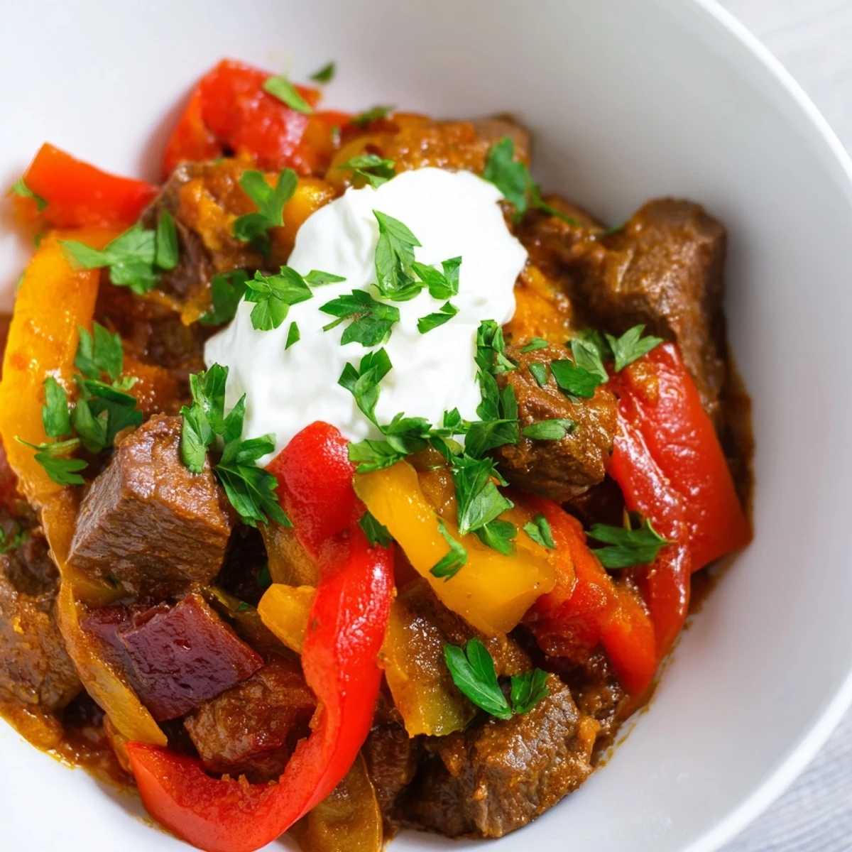 Hearty Rich Beef Goulash with Bell Peppers stewed in a red paprika sauce, served steaming in a rustic bowl with a fresh parsley garnish.