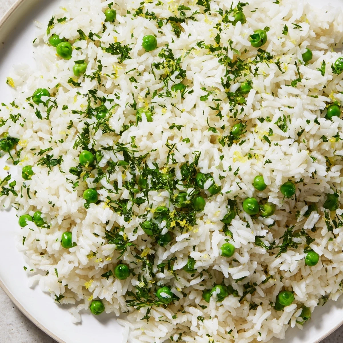 Fluffy Lemon Herb Rice Pilaf with sweet green peas, served in a white bowl, garnished with fresh herbs.