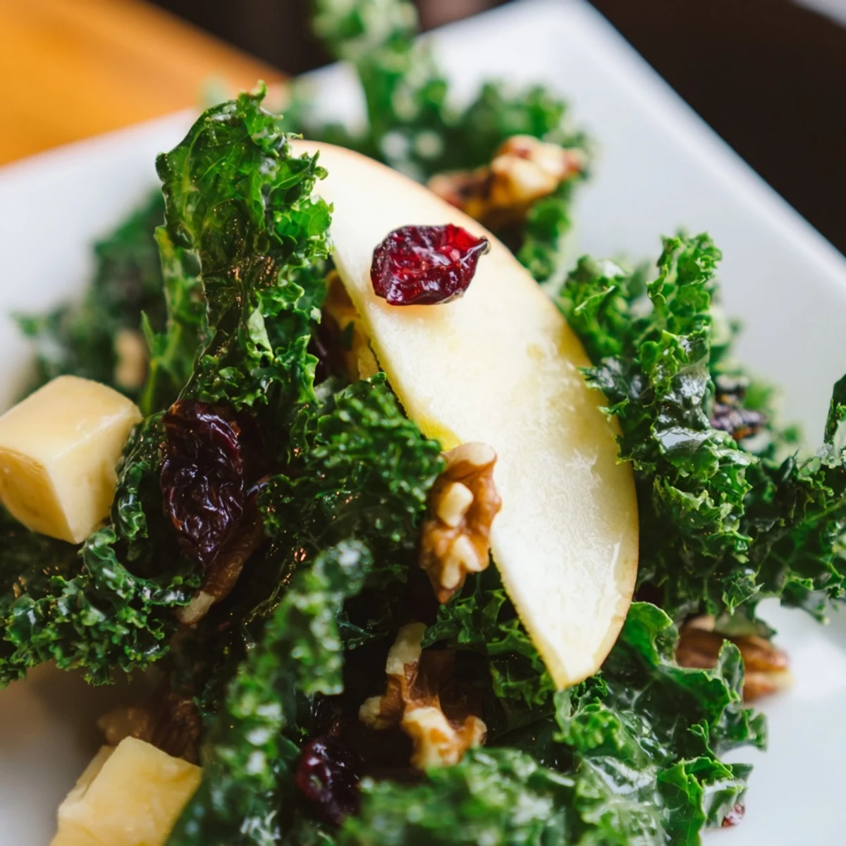 A close-up of Winter Kale Salad with Apple and Sharp Cheddar, featuring glistening kale, bright apple slices, and cubed cheddar with toasted walnuts.