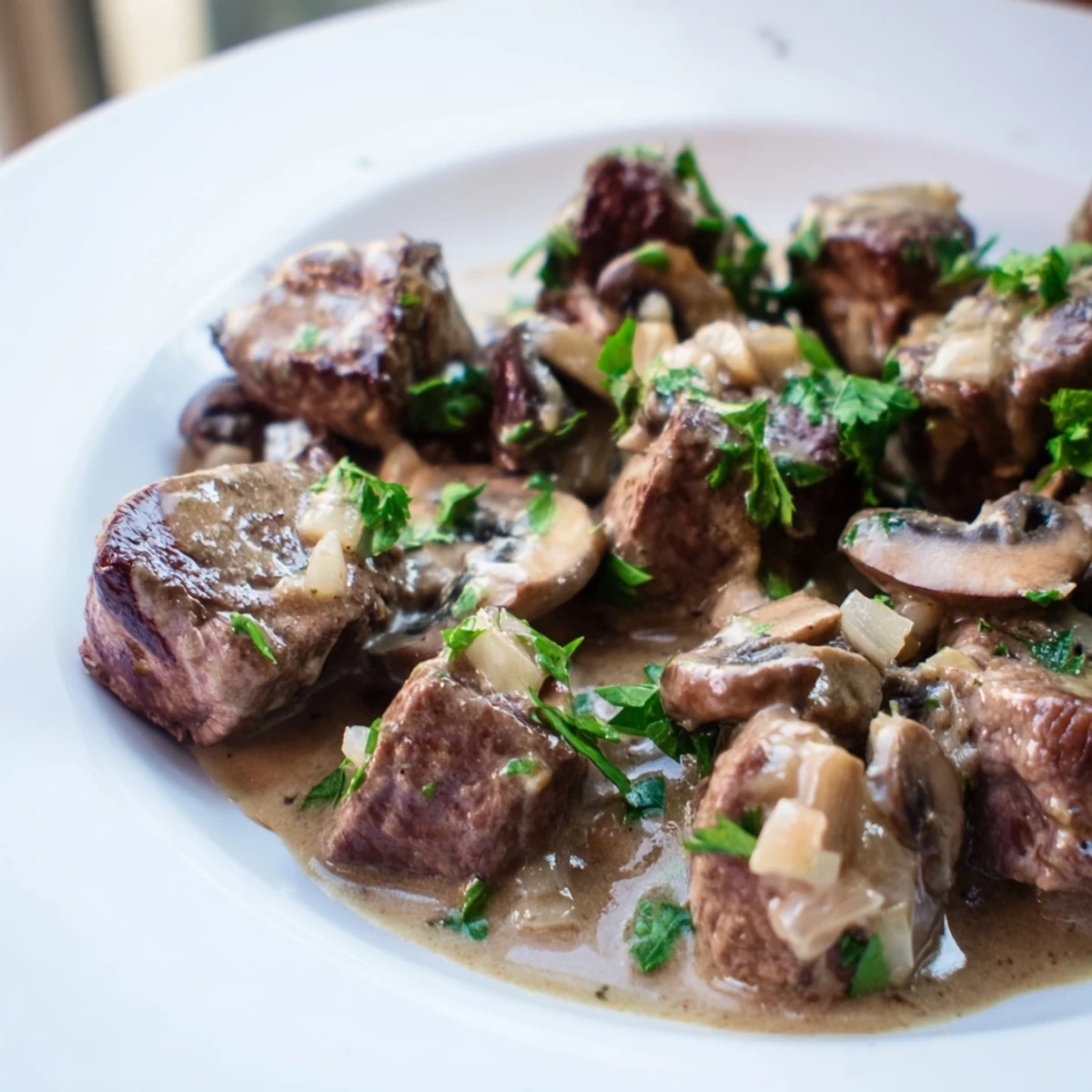 Tender steak bites in a rich mushroom sauce garnished with fresh parsley, perfect for a skillet meal.