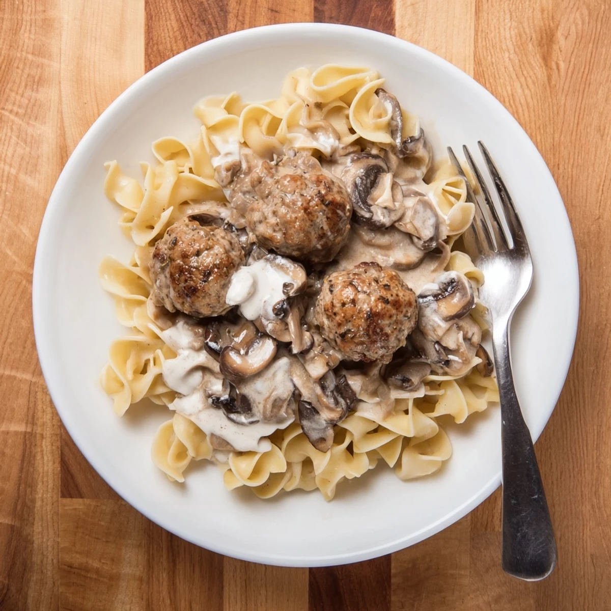 Golden-brown turkey meatballs nestled in a creamy mushroom stroganoff sauce, spooned over tender egg noodles on a rustic plate.