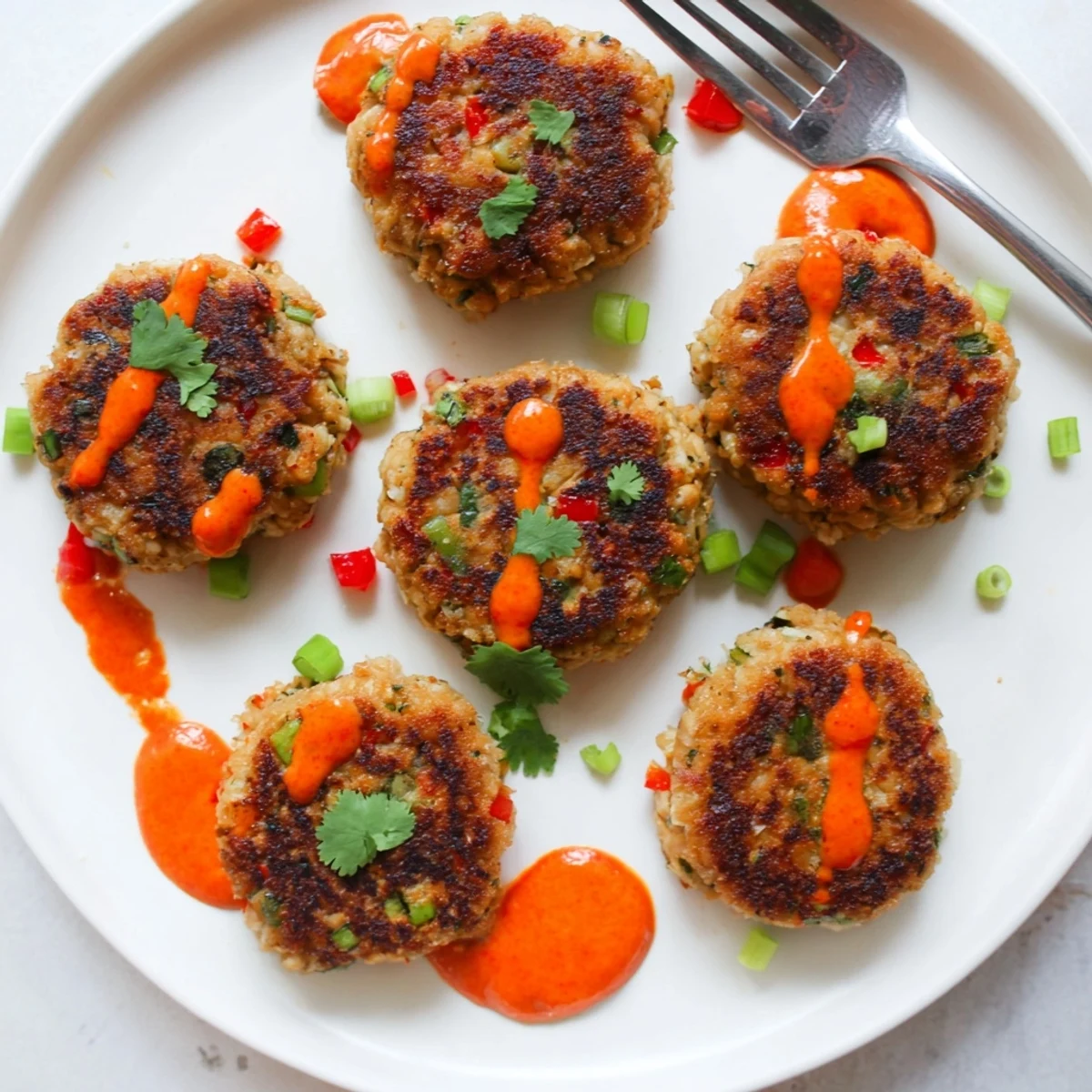 Overhead shot of golden Spicy Tuna Cakes with Sriracha Mayo served alongside lime wedges and fresh cilantro on a rustic wooden table.