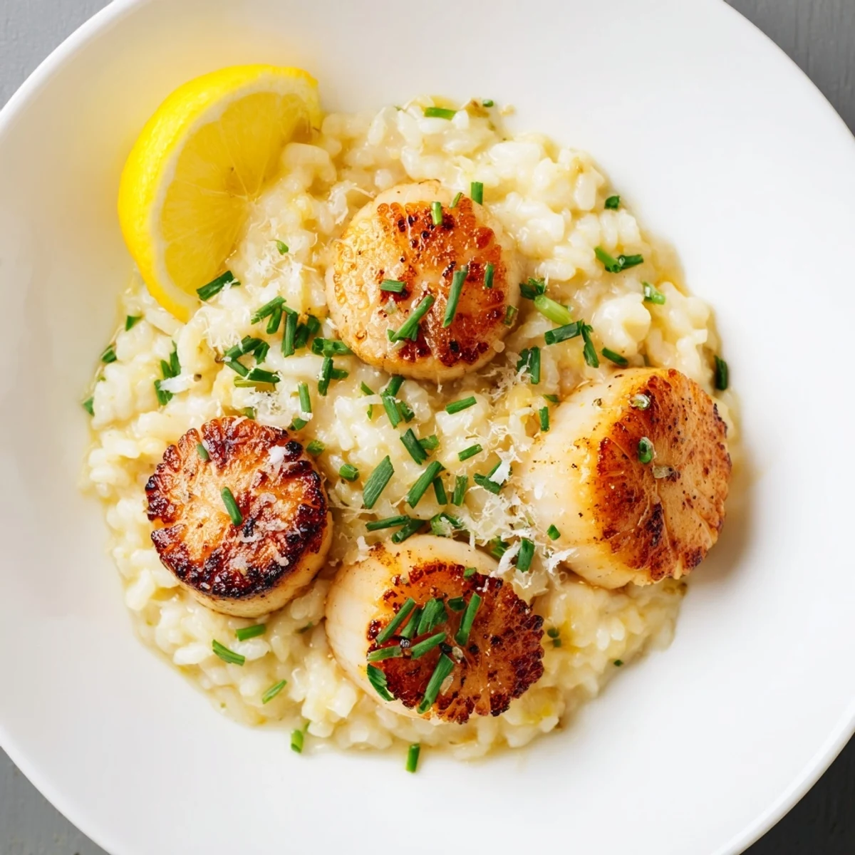 Golden-brown pan seared scallops resting on creamy lemon butter risotto, garnished with fresh chives and lemon wedges.  