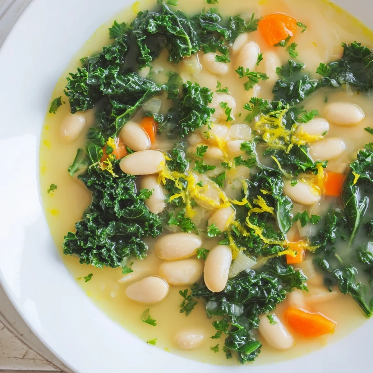 A steaming bowl of White Bean and Kale Soup with Lemon Zest shows creamy beans and wilted greens, garnished with fresh parsley.