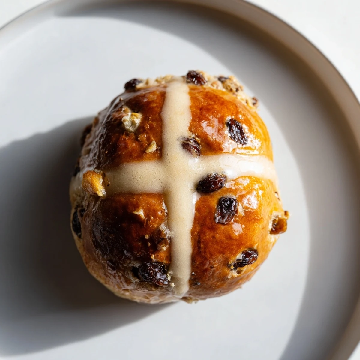 Golden brown Hot Cross Buns with Currants and Spices on a cooling rack, brushed with shiny glaze.
