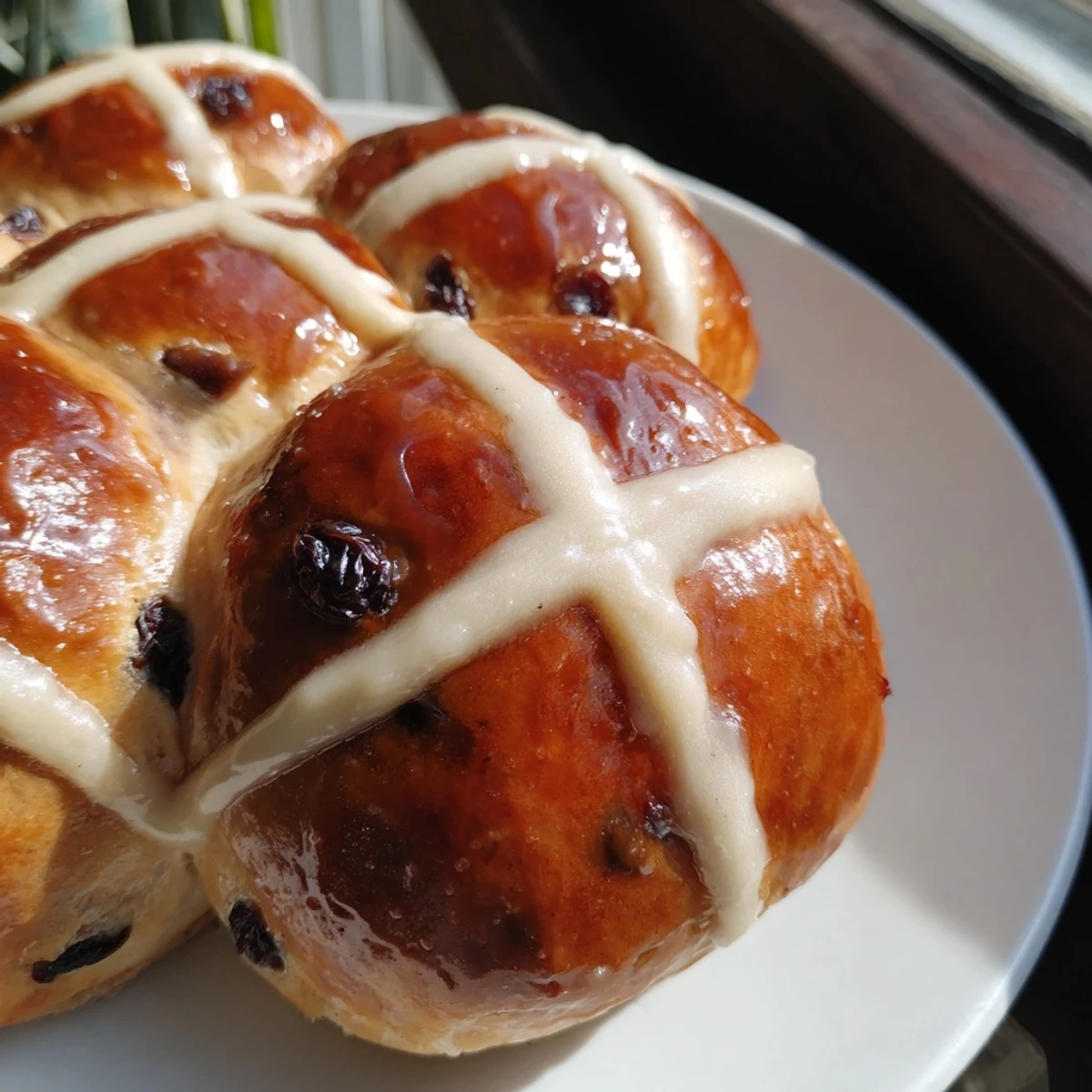 A warm plate of Hot Cross Buns with Currants and Spices, showcasing their soft, golden-brown texture and classic white piped cross.