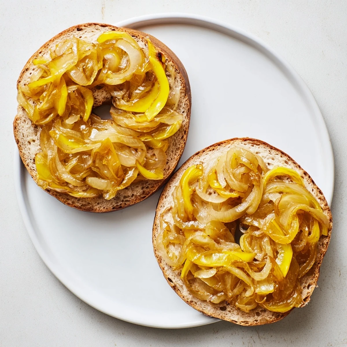 Warm Sourdough Onion Bagels sliced to reveal a chewy interior, served with a bowl of cream cheese for spreading.