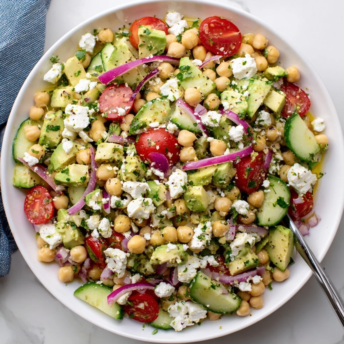 Freshly tossed Chickpea Feta Avocado Salad in a white bowl, featuring creamy avocado chunks, crumbled feta, cherry tomatoes, and cucumber with a lemon dressing.