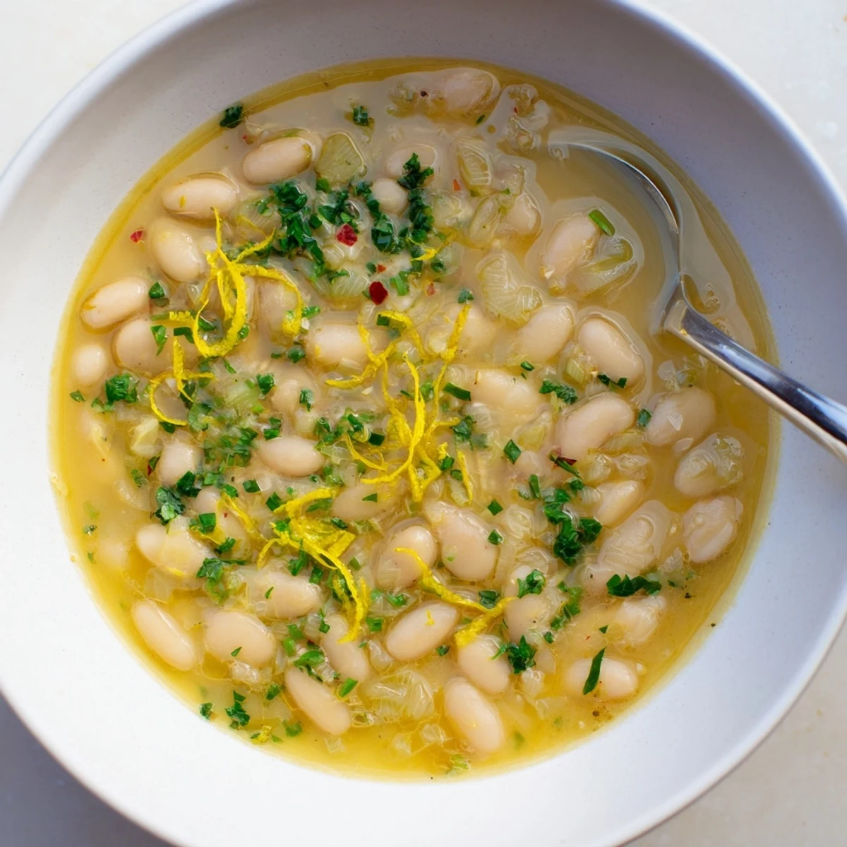 Steaming Miso Butter Brothy Beans served over steamed rice, with a drizzle of olive oil and bright herbs.