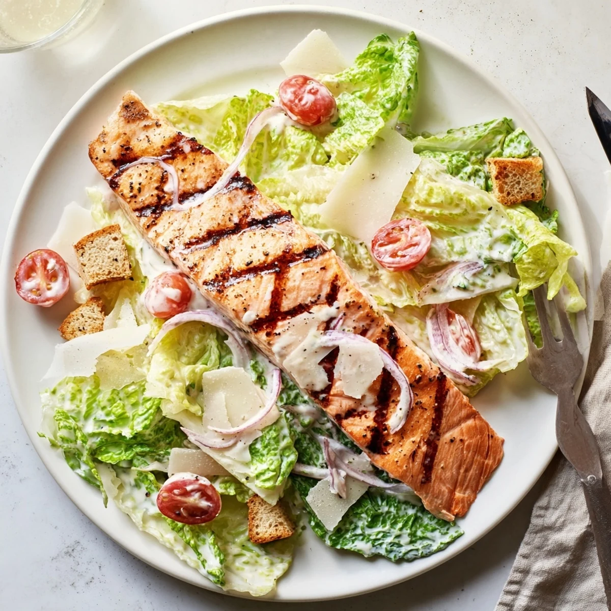 A close-up of Salmon Caesar Salad features flaky salmon, cherry tomatoes, and creamy homemade dressing drizzled over greens.