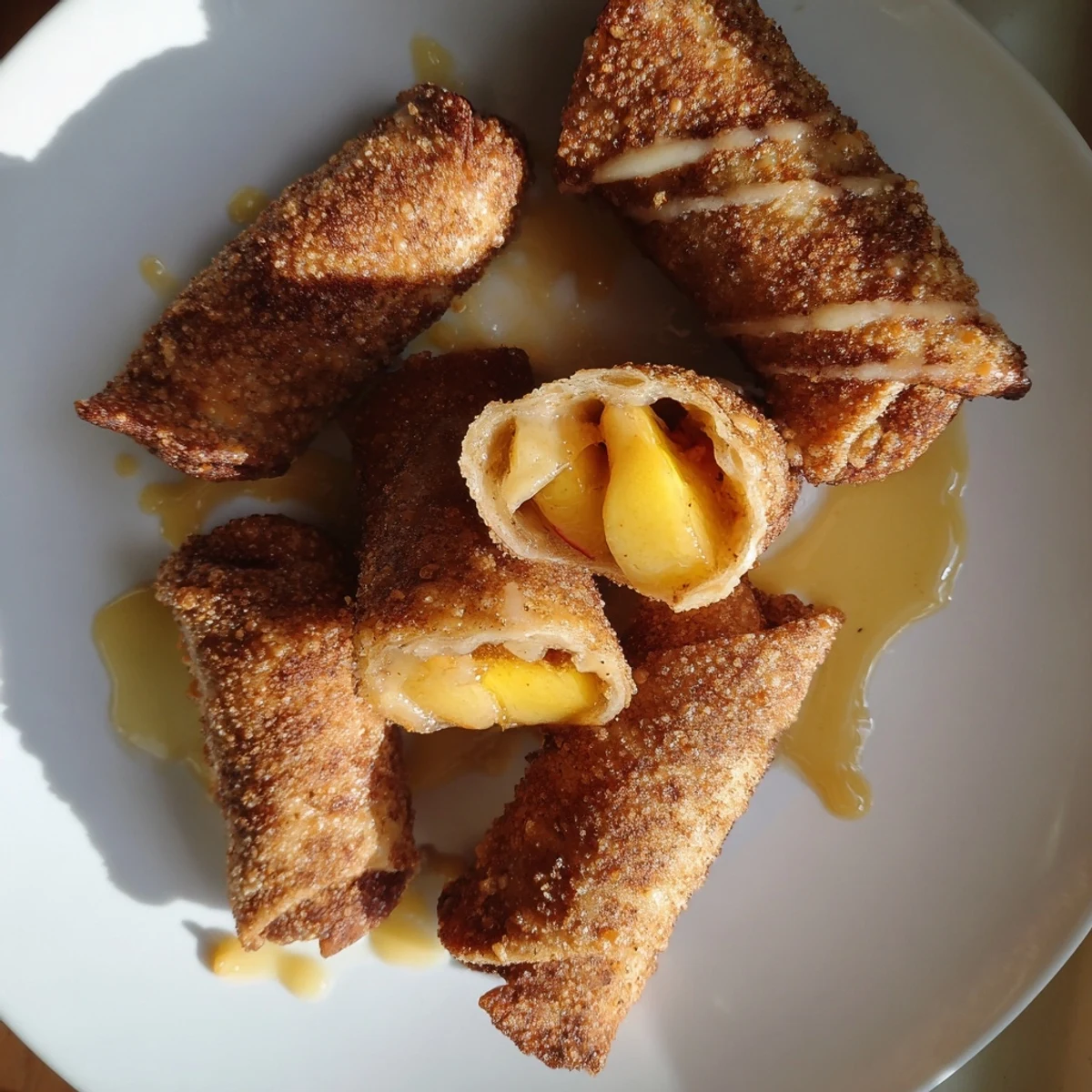 Plated Peach Cobbler Egg Rolls with vanilla glaze and a scoop of ice cream on a blue ceramic dish.