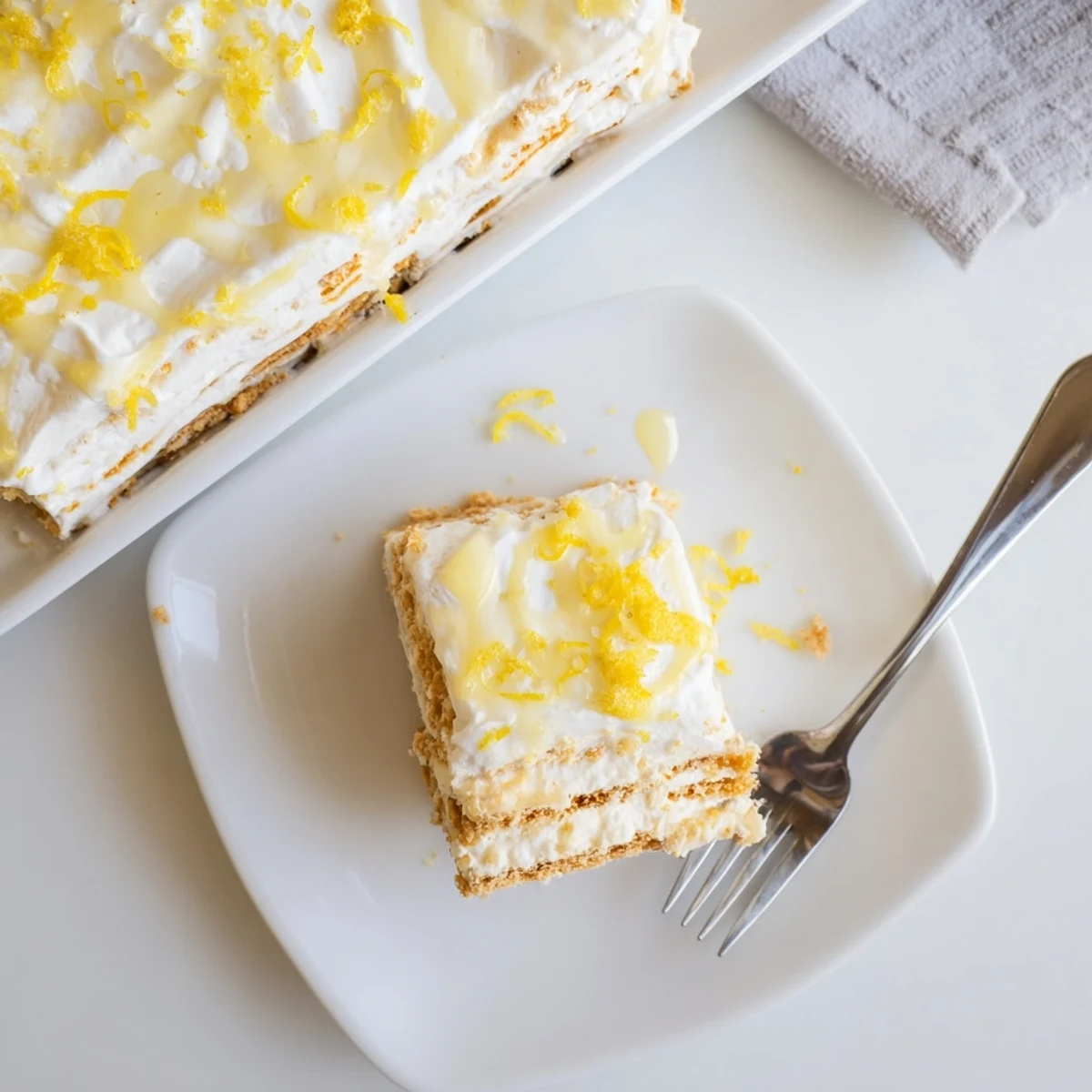 Summer No Bake Lemon Eclair Cake served in a glass dish with whipped cream and blueberries.