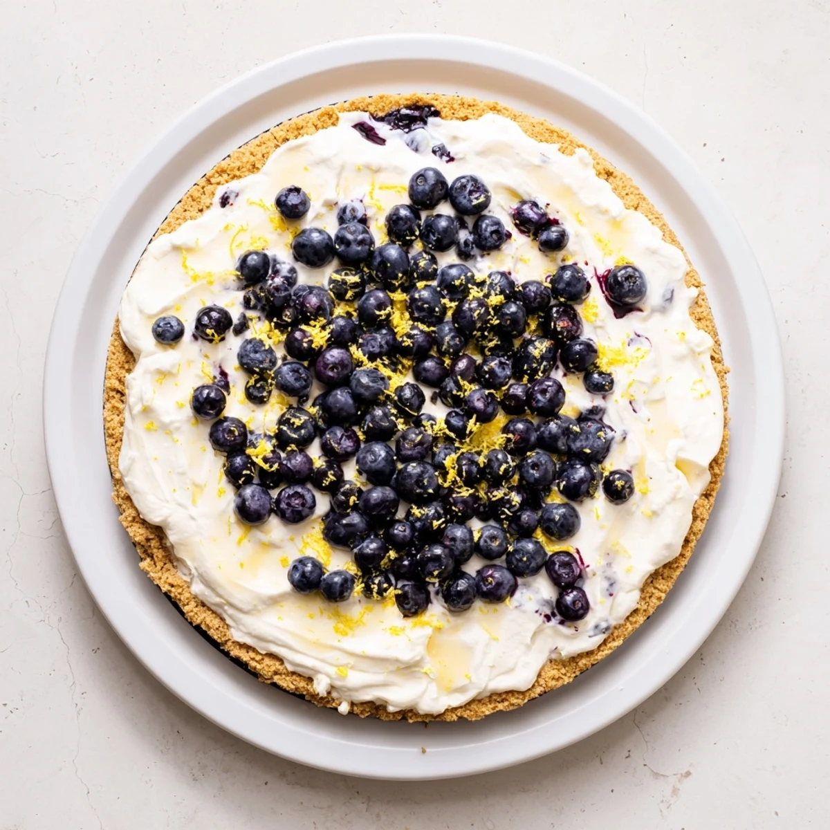 Close up view of No Bake Lemon Blueberry Cream Cake reveals creamy layers, graham crumbs, and glossy lemon zest garnish for serving.