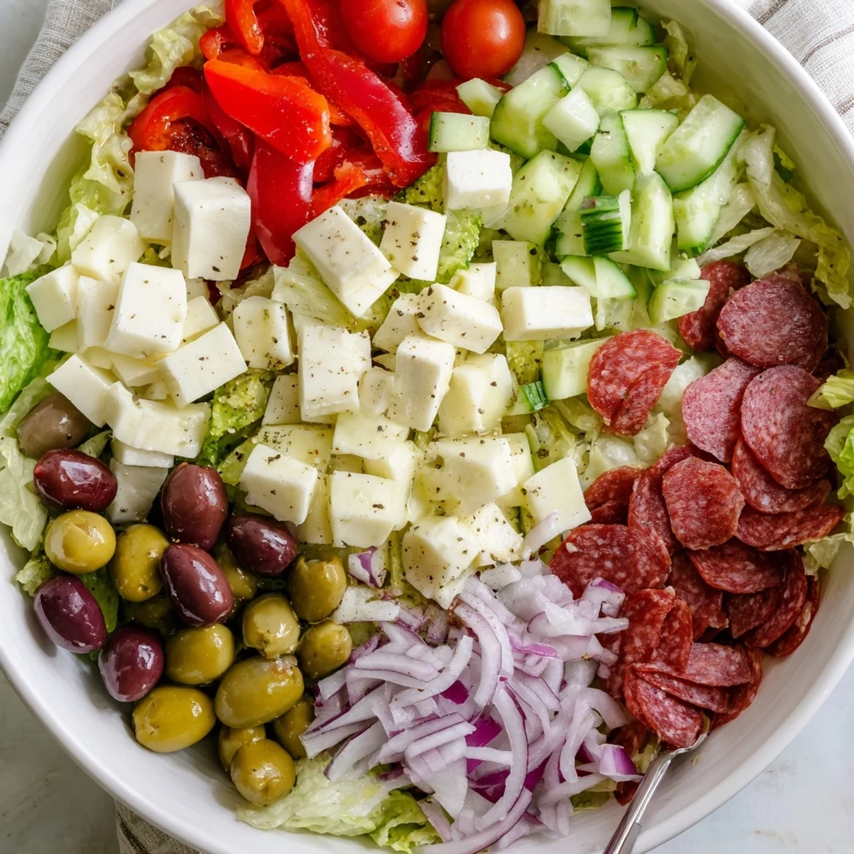 Mediterranean-style Italian chopped salad featuring crisp lettuce, tomatoes, olives, mozzarella, and savory cured meats drizzled with dressing