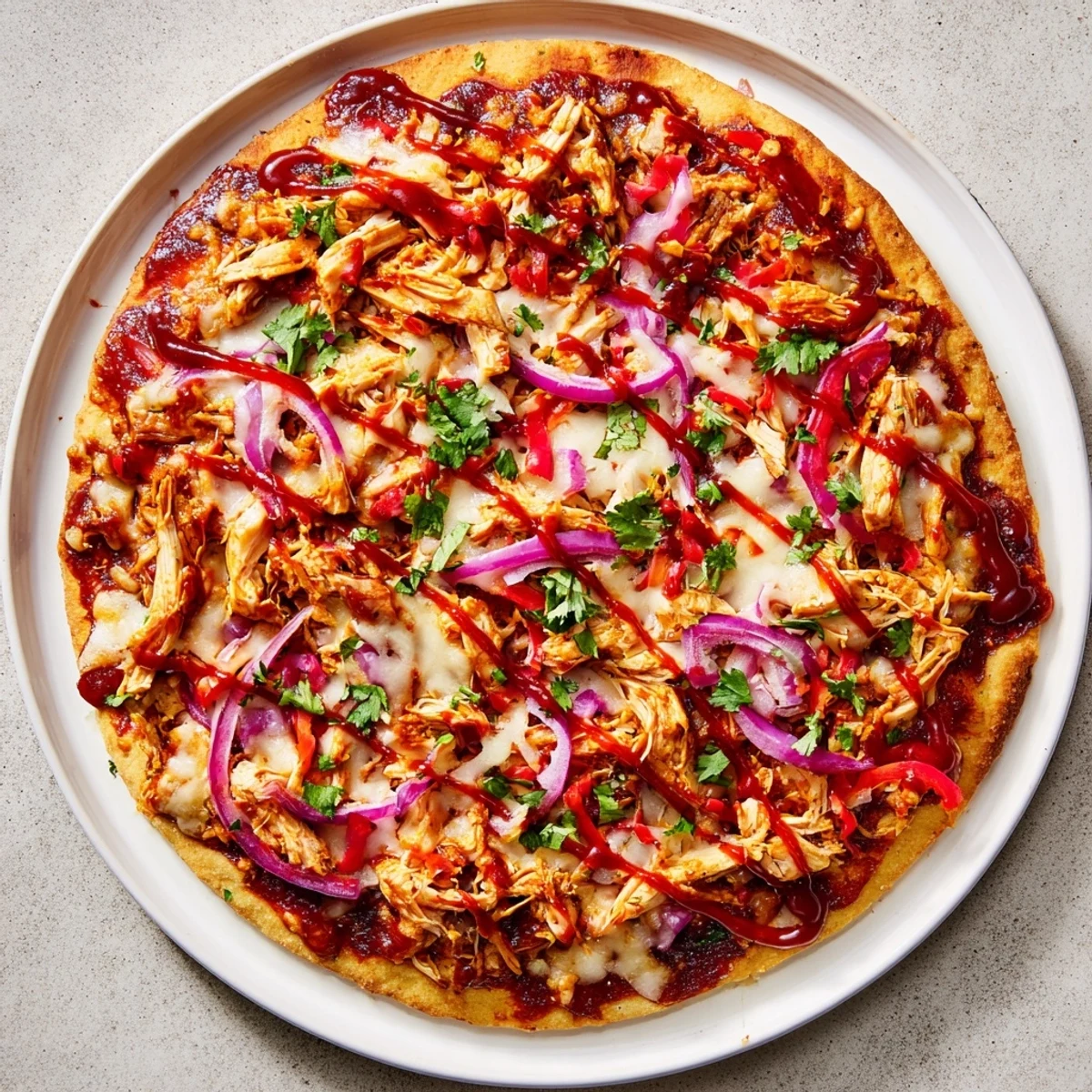 Sliced homemade BBQ chicken pizza drizzled with extra sauce featuring tender chicken, red onions, and bubbling mozzarella cheese