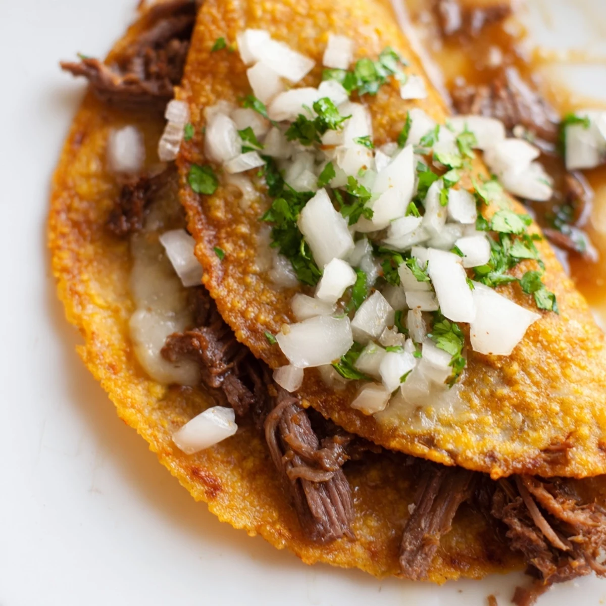 Golden pan-fried birria tacos stuffed with tender shredded beef, topped with diced onion and served alongside rich red dipping sauce