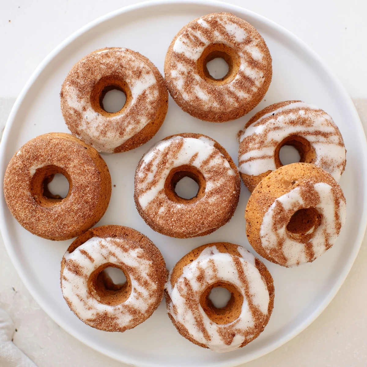 Golden brown pumpkin spice biscuit donuts coated in cinnamon sugar with sweet white glaze drizzle