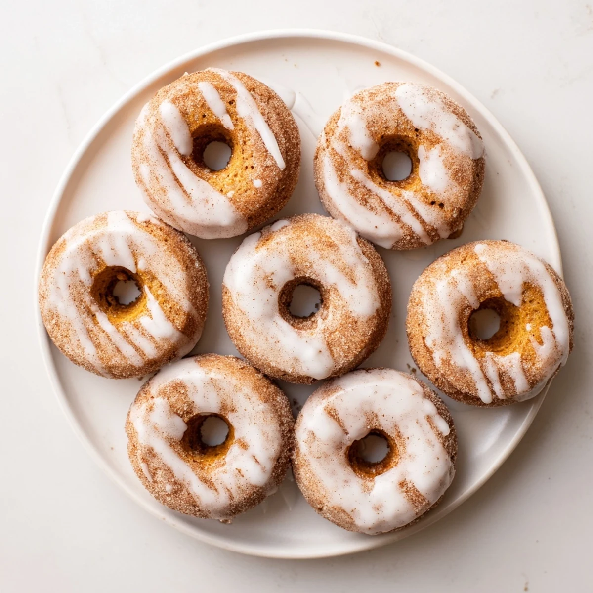Warm pumpkin spice biscuit donuts with glossy vanilla glaze resting on a wire cooling rack