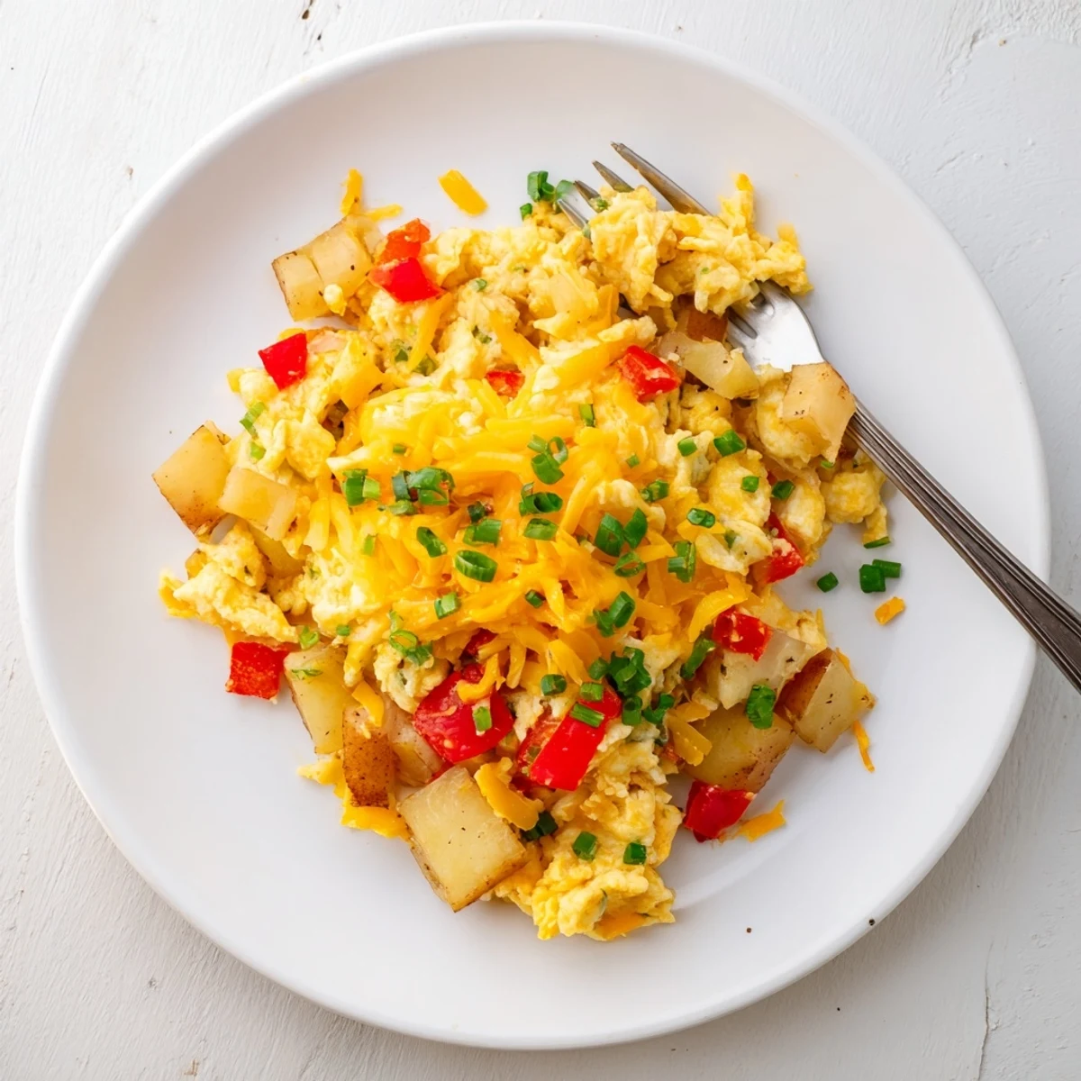 Golden cheesy potato egg scramble in a cast iron skillet with melted cheddar