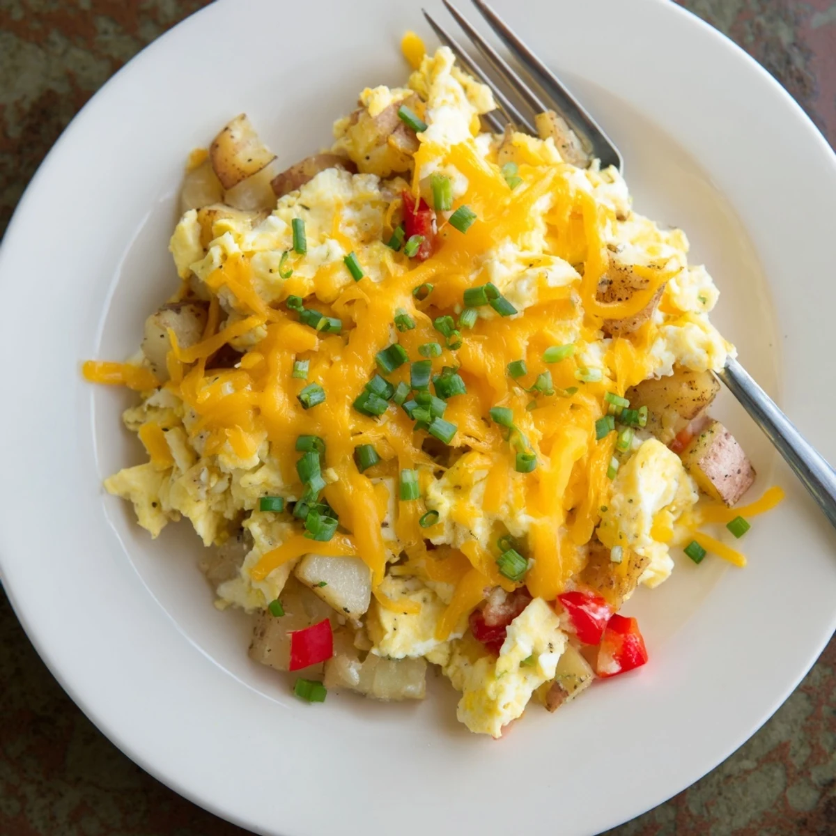 Fluffy scrambled eggs with crispy potatoes and cheese served on a white plate