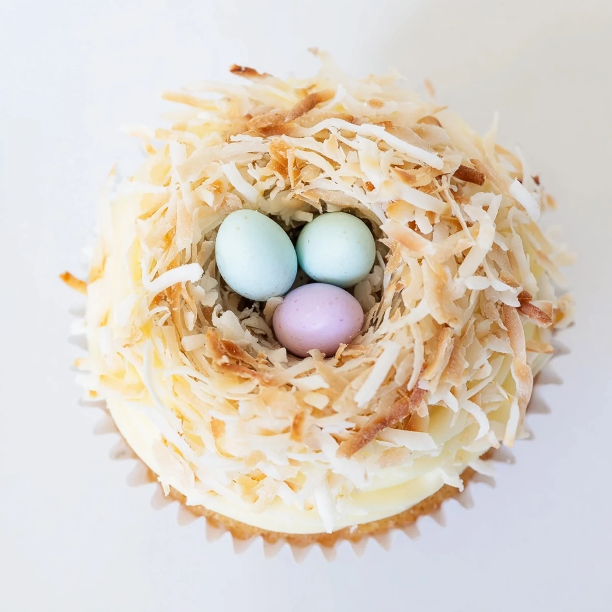 Homemade coconut nest cupcakes topped with whipped coconut frosting and sweet chocolate egg candies