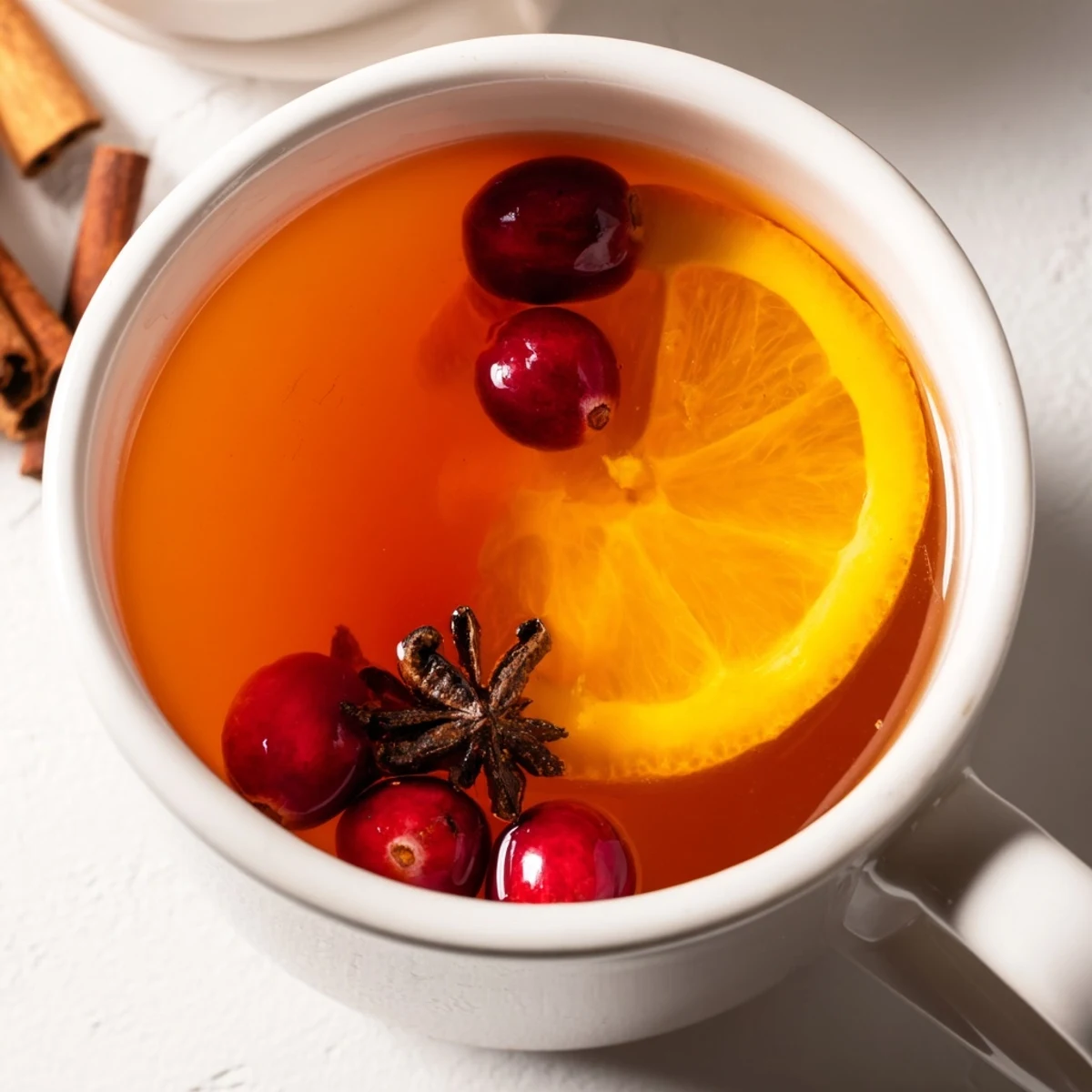 Golden Orange Cranberry Tea with red cranberries and orange slices simmering in copper saucepan with steam rising