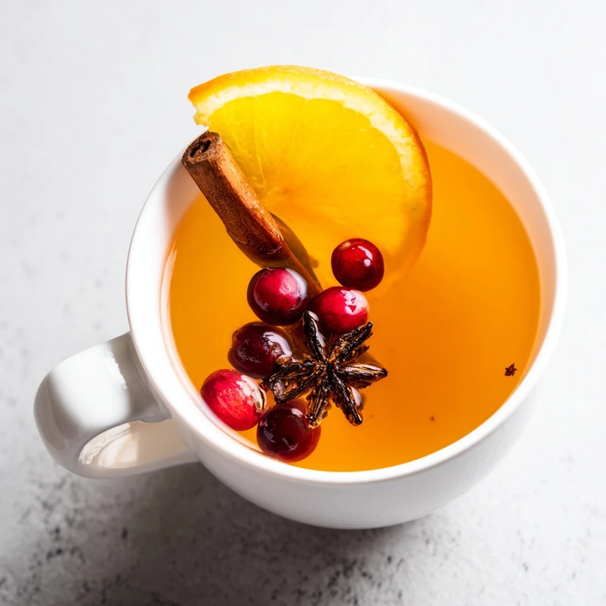 Rustic mug of hot Orange Cranberry Tea garnished with orange wheel and star anise on wooden table