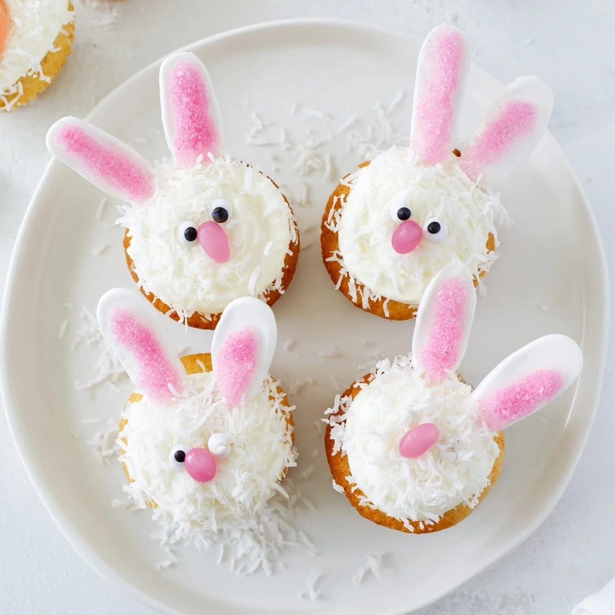 Adorable bunny cupcakes with pink glitter ears and jelly bean noses on coconut-covered frosting.