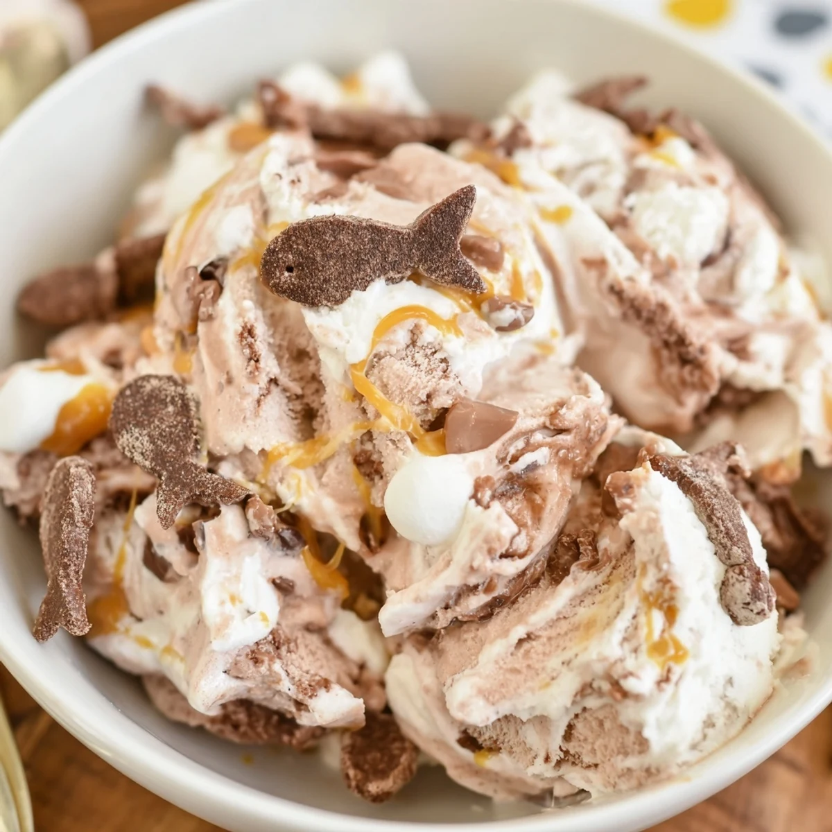 Creamy Ninja Creami Phish Food ice cream swirled with marshmallow fluff, caramel ribbons, and chocolate fish in a chilled glass bowl