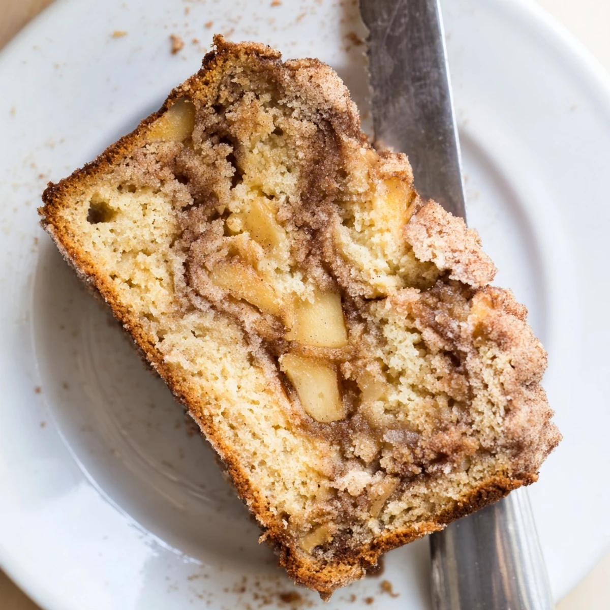 Golden brown cinnamon apple bread loaf with visible apple chunks and a sugary cinnamon swirl top
