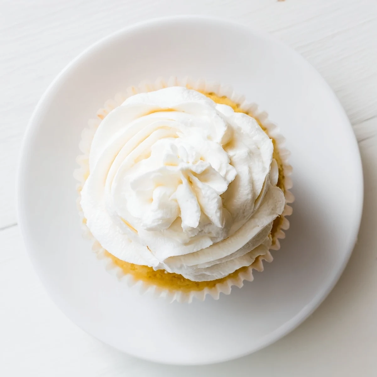 Golden vanilla cupcakes topped with fluffy swirls of creamy white buttercream frosting on a white plate