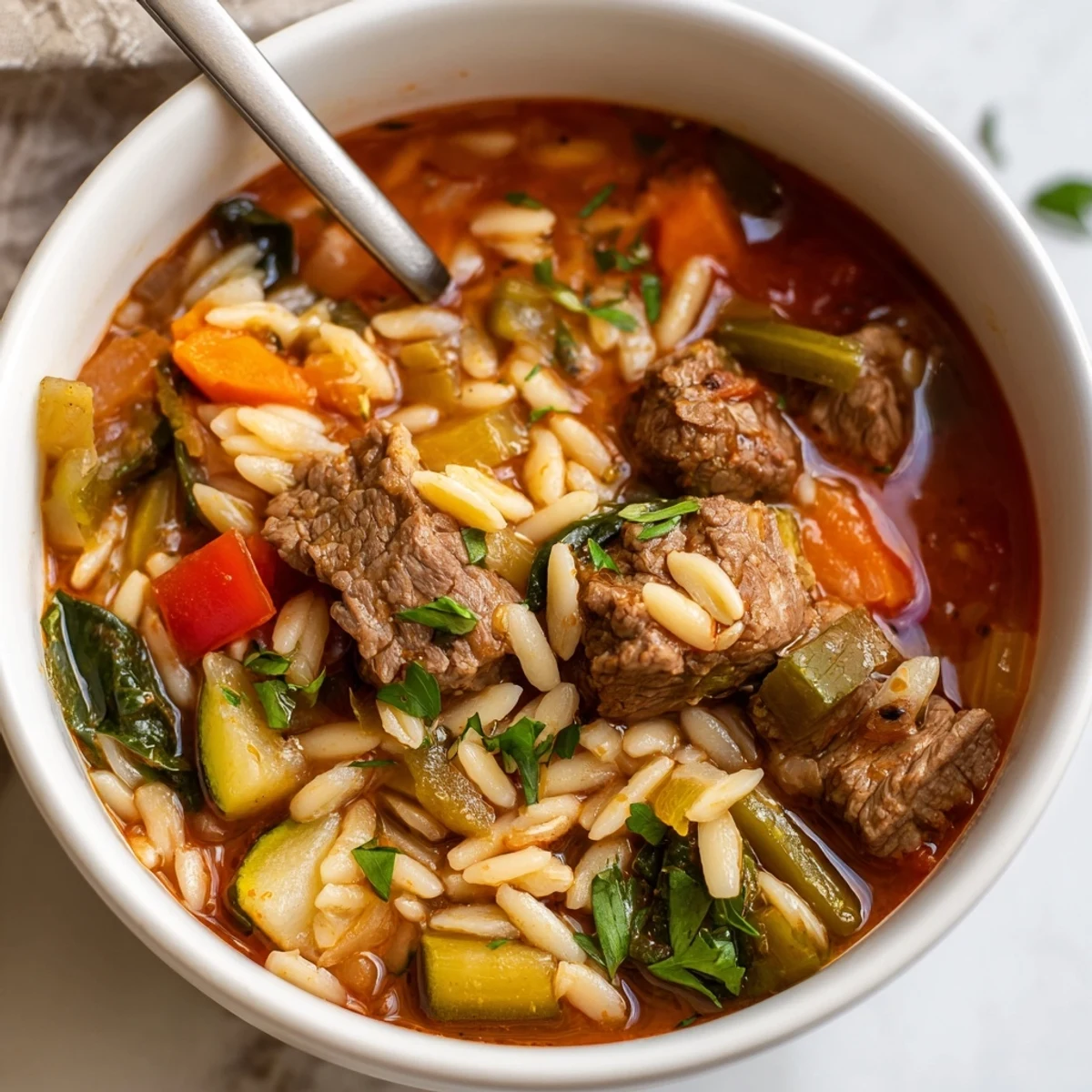 Steaming bowl of Hearty Beef and Orzo Soup with tender meat and colorful vegetables