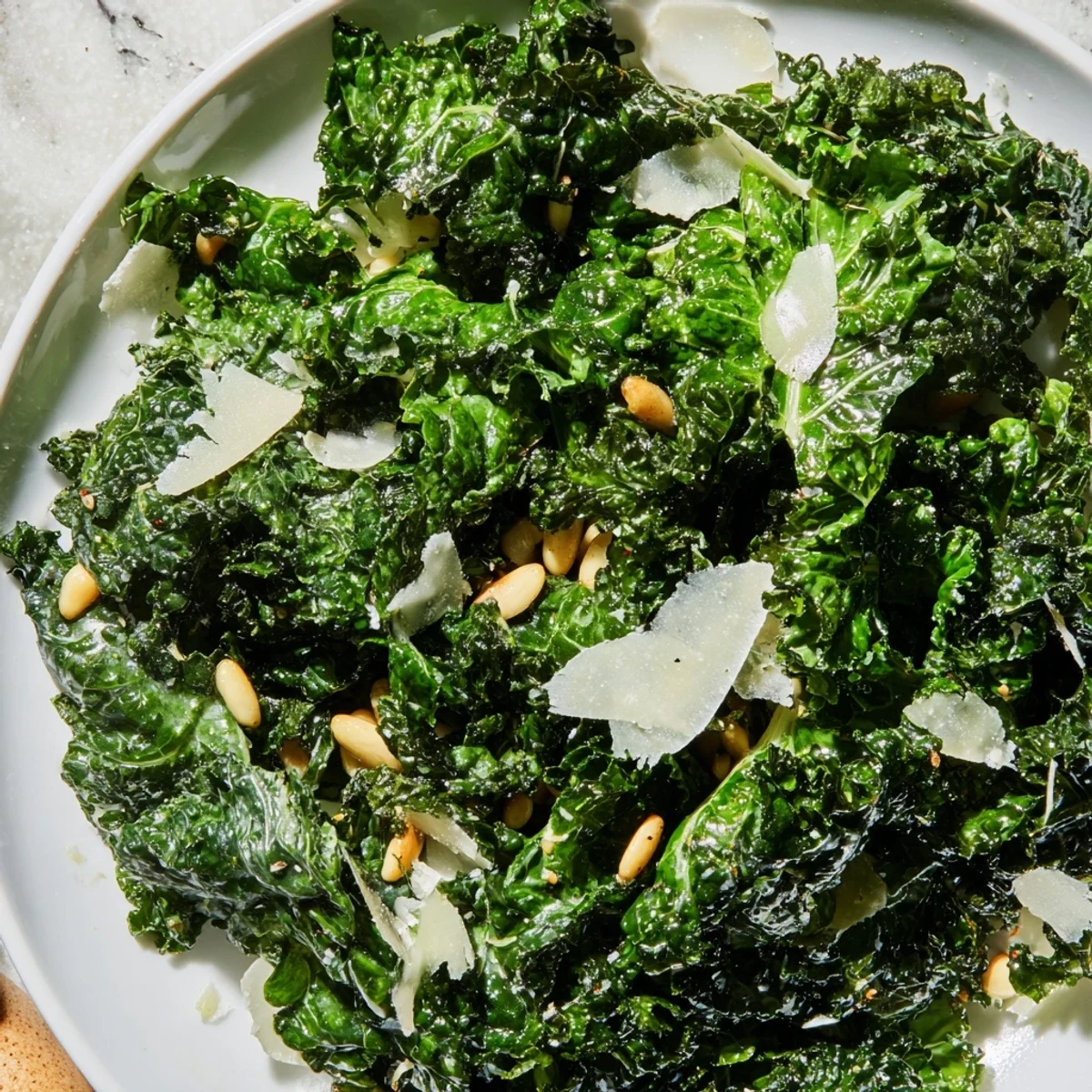 Bright garlic lemon Parmesan kale salad topped with toasted pine nuts and shaved cheese