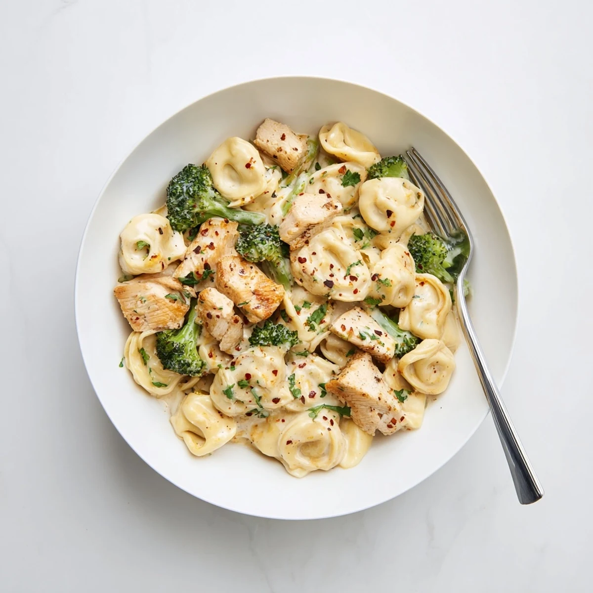 Creamy Garlic Parmesan Tortellini Chicken Broccoli plated with steaming sauce and parsley.