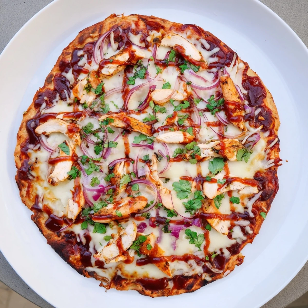 Sliced grilled BBQ chicken pizza topped with tangy sauce, red onions, and bubbling cheese on a charcoal-grilled base