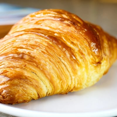 A close-up of gluten-free croissants beside a cup of coffee for breakfast.